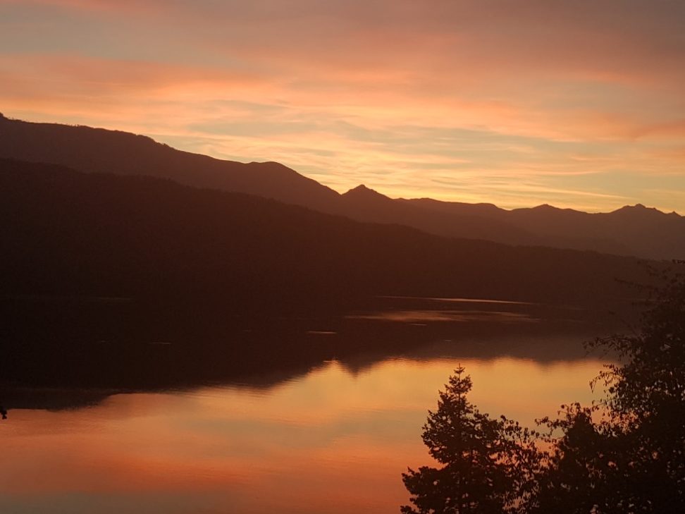 Sonnenuntergang am See Sonnenuntergang über einem ruhigen See, umgeben von Bergen und buntem Himmel.